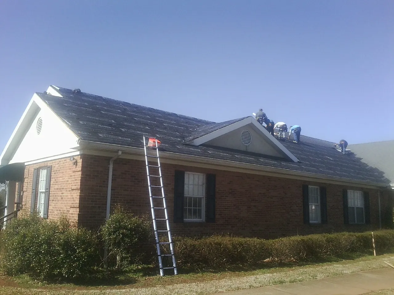 Crew tearing shingles off a brick ranch roof with a ladder set — Metal Roof Repair work by our crew in Coupland