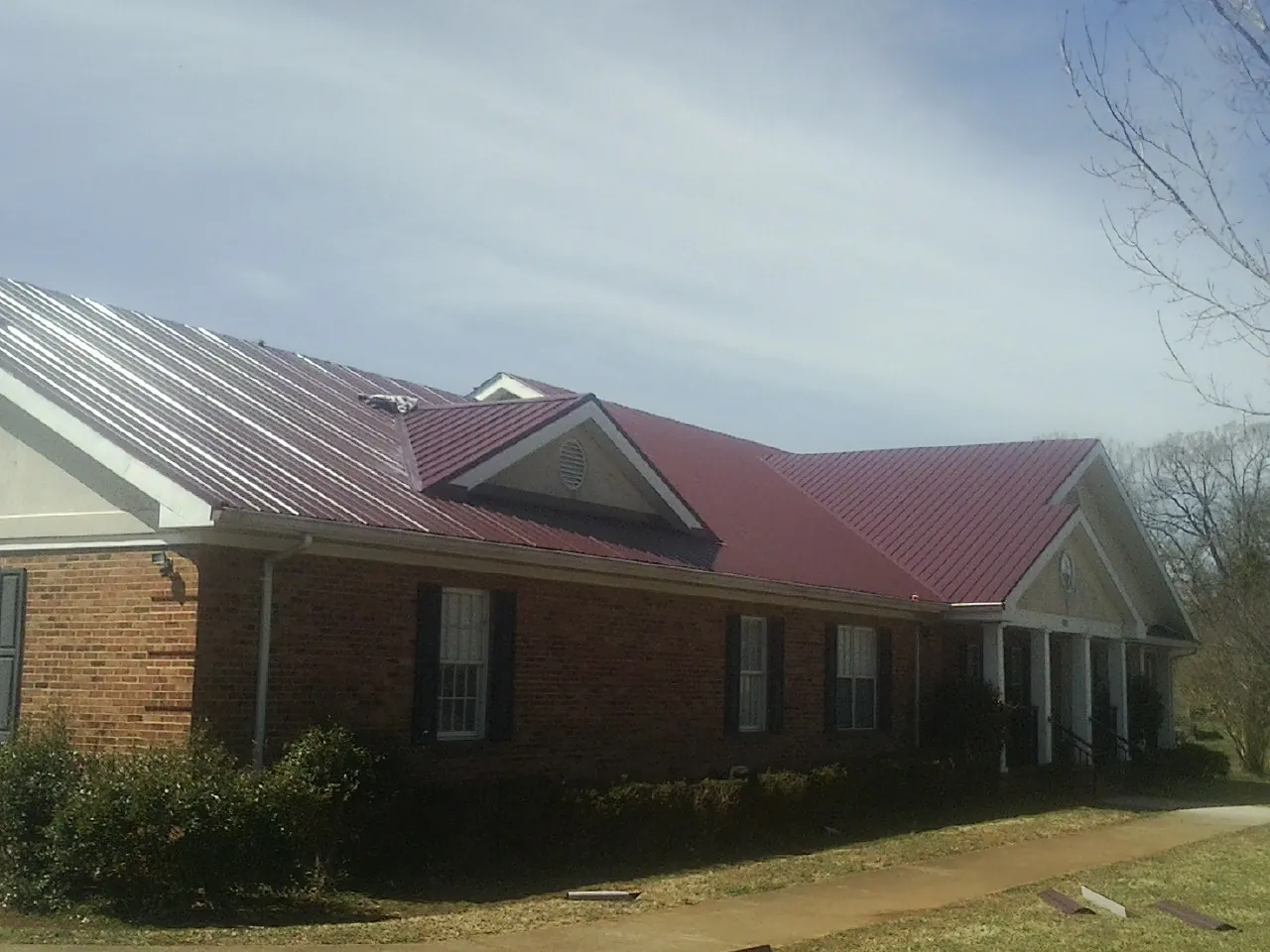 Red metal roof with gabled entries on a long brick building, from a Hail Damage Roof Repair job in Coupland