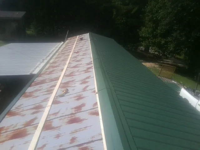 Old rusted panels beside newly installed green metal roofing — Wind Damage Roof Repair by Roofing Brothers in Coupland