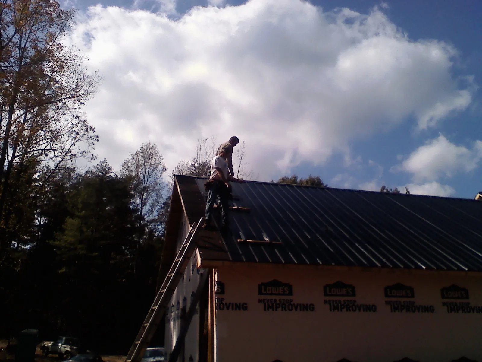 Roofer fastening dark metal panels high against a cloudy sky, from a Roof Inspection job in Coupland
