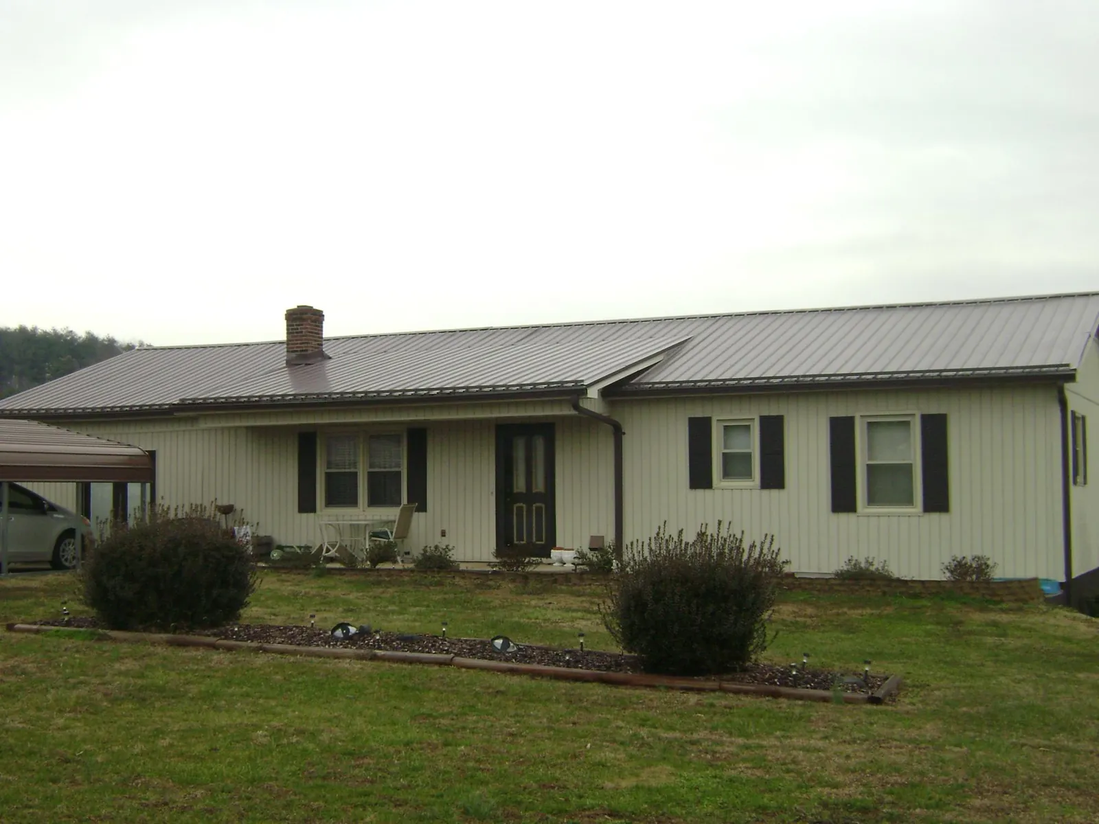 Brown metal roof on a cream sided ranch home with a brick chimney in Coupland
