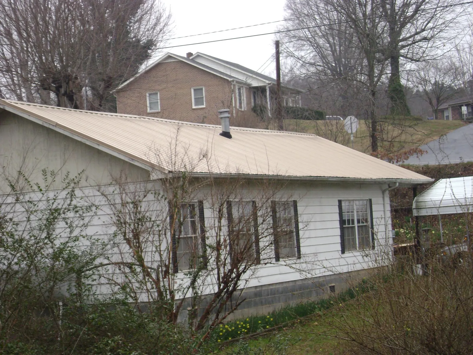 Tan metal roof on a white sided house set into a hillside — Commercial Roofing by Roofing Brothers in Coupland