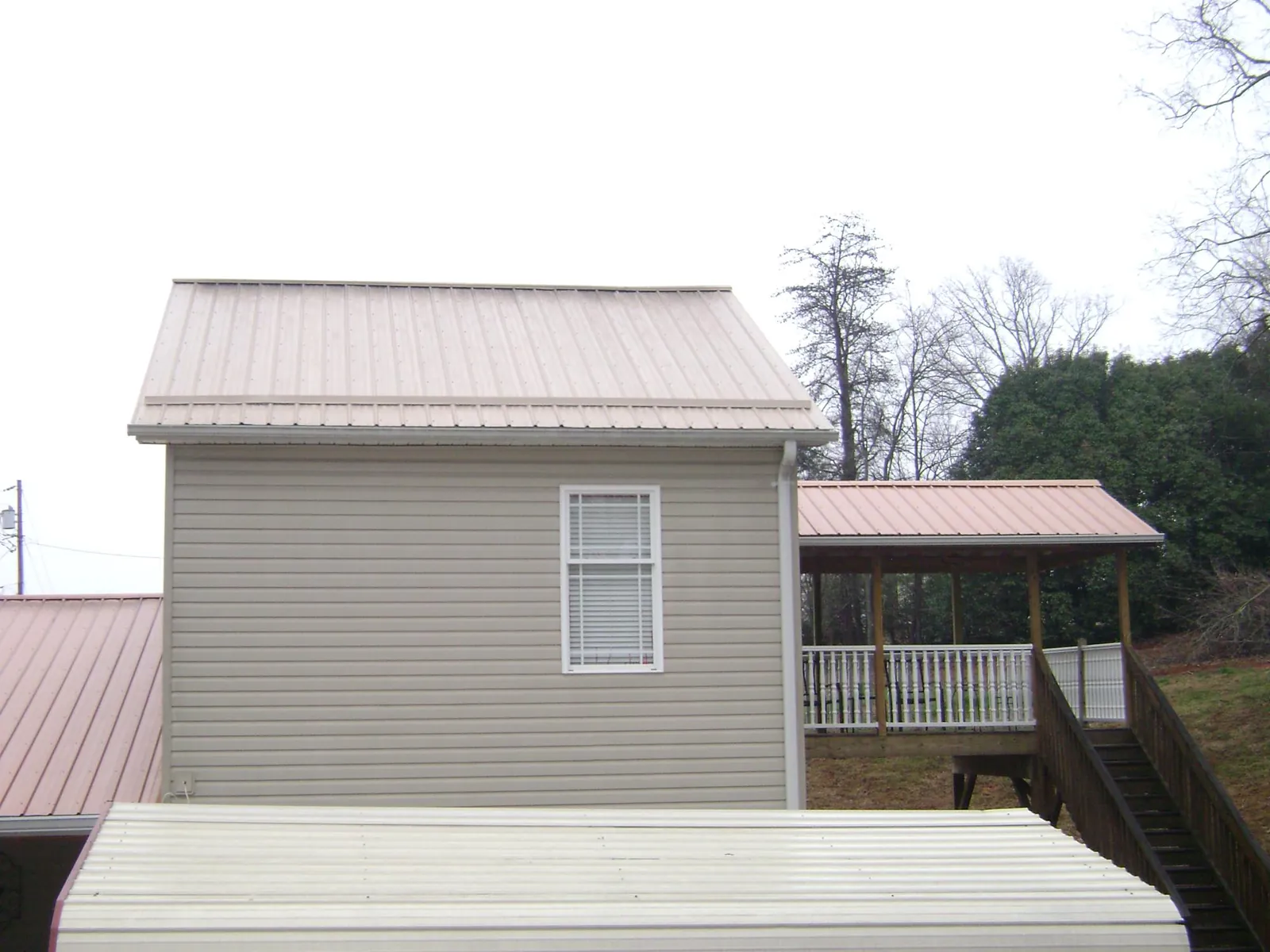 Tan metal roofs on a two story addition and attached porch, from a Roof Replacement job in Coupland